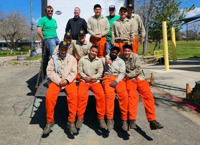 A group of youth conservation camp crewmembers pose behind a large truck.